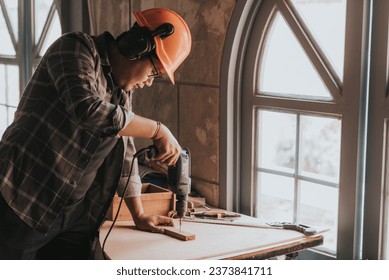 a Young man Carpenter works on woodworking machinery in a carpentry shop. The workshop looks professional, highly skilled, and the craftsmen are true craftsmen. - Powered by Shutterstock