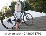 young man carries a bicycle up a set of concrete stairs in a park setting