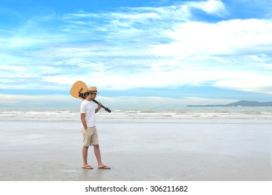 Young Man Carrying Guitar Walking On The Beach