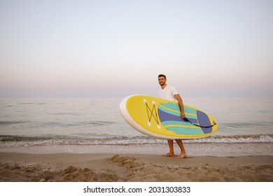 Young Man Carrying Sup Board After Water Surf Session