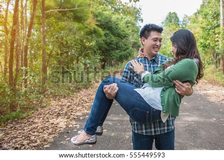 A young man carrying a young woman on the street in the park.
