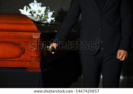 Young man carrying wooden casket in funeral home, closeup