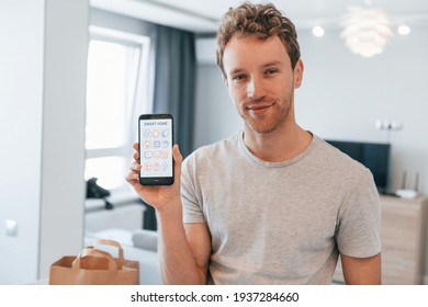 Young Man In Casual Clothes Is Indoors Controlling Smart Home Technology.