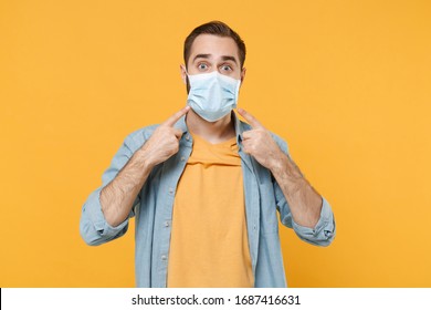 Young man in casual clothes posing isolated on yellow background studio portrait. Epidemic pandemic coronavirus 2019-ncov sars covid-19 flu virus concept. Pointing index fingers on sterile face mask