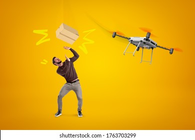 Young Man In Casual Clothes Trying To Catch Cardboard Box Dropped Off Delivery Drone On Amber Background. Drone Delivery Service. Retail Delivery. Modern Technologies.