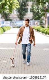 Young Man In Casual Clothes Walking With Jack Russell Terrier Dog Along City Alley