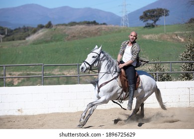 Young Man In Casual Outfit Riding White Horse On Sandy Ground