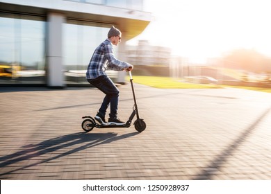 Young man in casual wear on electric kick scooter on city street in motion blur in sunday