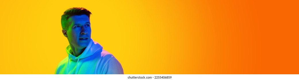 Young man in casual white hooding posing  looking away isolated over gradient yellow orange background in neon light  Banner  flyer  Concept emotions  facial expression  sales  ad  fashion