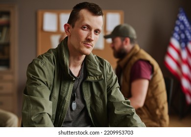 Young Man In Casualwear Sitting In Front Of Camera After Psychological Session Against Other Attendants Of PTSD Support Group