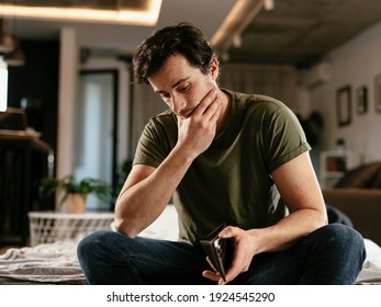 Young Man Checking Empty Wallet, No Money. Unemployed Sad Man Sitting At Home Thinking About Money.