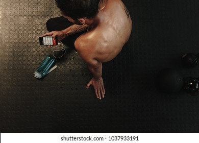 Young Man Checking Fitness Progress On His Smart Phone. Top View Of Muscular Male Looking At His Workout Performance On Mobile Phone.