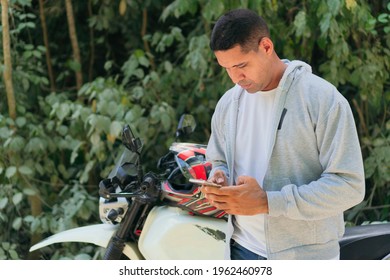 Young man checking his cell phone before taking a motorcycle ride in the countryside in summer.