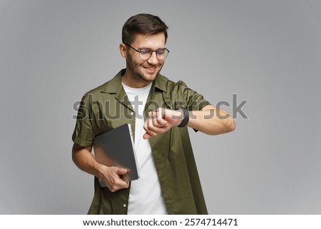 Young man checking smartwatch while holding a laptop in a modern indoor setting
