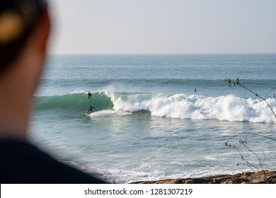 A Young Man Checking The Swell While A Surfer Is Catching A Wave At Iconic Anchor Point, The Most Famous Surf Spot In Morocco. 