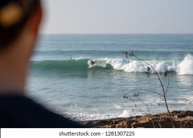 A Young Man Checking The Swell While A Surfer Is Catching A Wave At Iconic Anchor Point, The Most Famous Surf Spot In Morocco. 