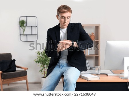 Young man checking time while sitting on table in office. Being late
