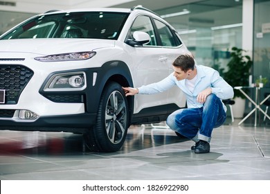 Young Man Checking Tires Of New Car In Dealership