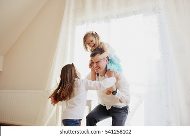 Der junge Mann verbringt fröhlich Zeit mit den kleinen Töchtern. Jüngeres Mädchen sitzt auf dem Vater auf den Schultern, ein anderes versucht den Vater zu besteigen. Kinder und Vater freuten sich über ein Stück.