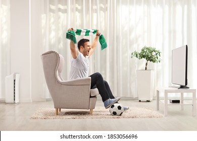 Young Man Cheering With A Scarf And Watching A Football Game On Tv At Home