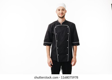 Young Man Chef In Black Uniform And White Cap Dreamily Looking In Camera Over White Background