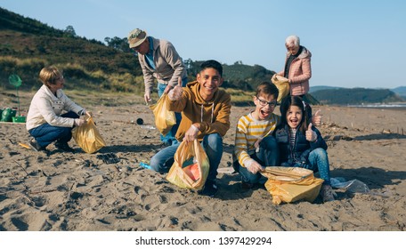 Young Man And Children Posing While Picking Up Trash With Group Of Volunteers On The Beach