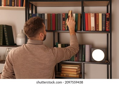 Young man choosing book on shelf in home library, back view - Powered by Shutterstock