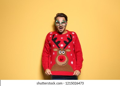 Young man in Christmas sweater with party glasses on color background