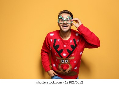 Young Man In Christmas Sweater With Party Glasses On Color Background