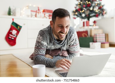 Young Man In Christmas Sweater Using Laptop And Drinking Coffee