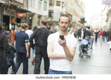 Young Man In City With Mobile Phone Walking, Background Is Blured City Street