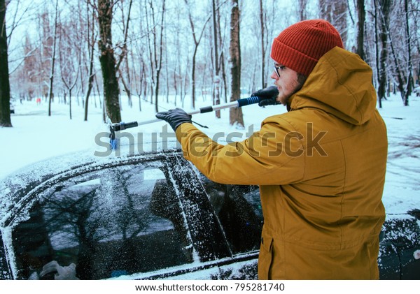 young man\
clean car after snow storm with\
scraper