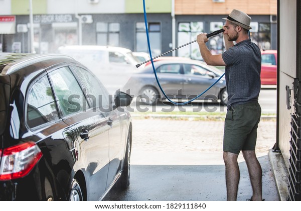Young man cleaning automobile with high pressure\
water jet at car wash