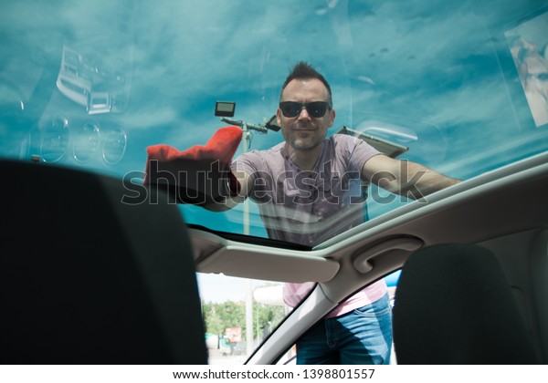 Young man cleaning\
glass roof on his car