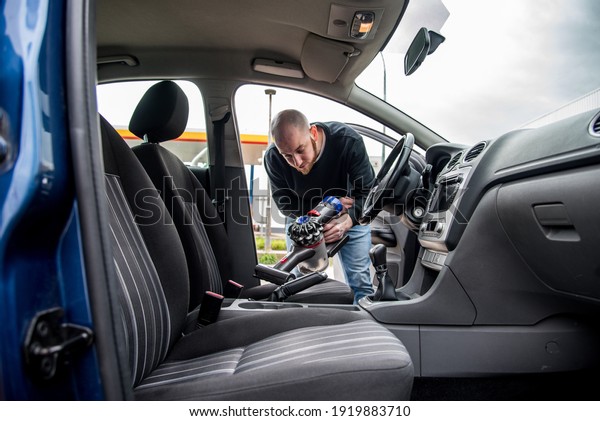 Young man cleaning the interior of a car\
using a  handheld portable vacuum\
cleaner.