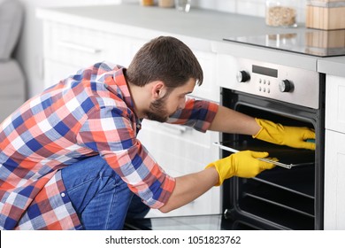 Young Man Cleaning Oven In Kitchen