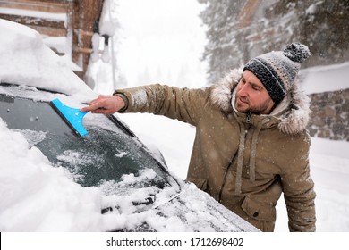 Young Man Cleaning Snow From Car Windshield Outdoors On Winter Day