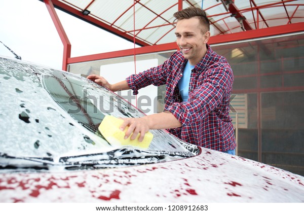 Young man cleaning vehicle with sponge at\
self-service car wash