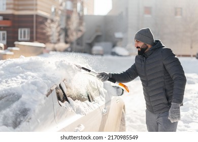 A young man cleans his car after a snowfall on a sunny, frosty day. Cleaning and clearing the car from snow on a winter day. Snowfall, and a severe snowstorm in winter. - Powered by Shutterstock