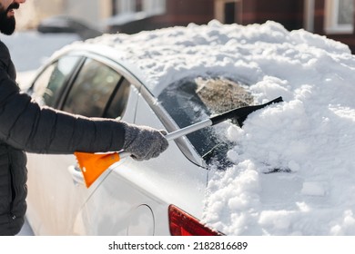 A young man cleans his car after a snowfall on a sunny, frosty day. Cleaning and clearing the car from snow on a winter day. Snowfall, and a severe snowstorm in winter. - Powered by Shutterstock