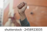 A young man clenches his fist in an empowering gesture on an urban street, symbolizing strength and determination.