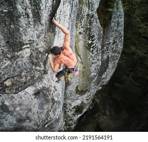 Young man climber climbing difficult route on high boulder with rope. Fearless rock climber training rock climbing on summer day. Concept of extreme sport, adventures and active lifestyle. Aerial