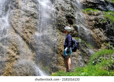 Young Man In Climbing Equipment Against Rock, Waterfall, Climbs Rock, Active Lifestyle Of People, Mountaineering, Via Ferrata In Mountains Of Alps, Life Insurance In Extreme Sports