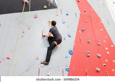 Young Man Climbing Indoor Wall And Reaching The Top