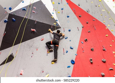 Young Man Climbing Indoor Wall And Reaching The Top