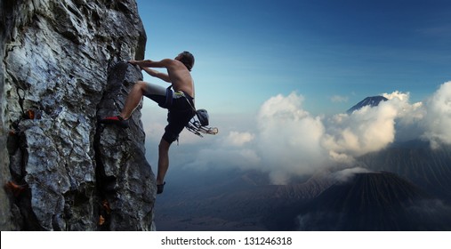 Young man climbing natural rocky wall with volcanoes on the background