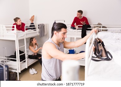 Young Man Climbing Up To Top Bunk Of Bunk Bed In Hostel Dorm