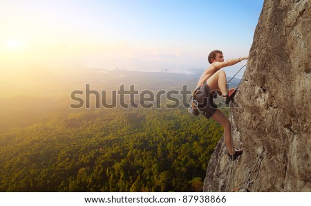 Young man climbs on a rocky wall in a valley with mountains at sunrise
