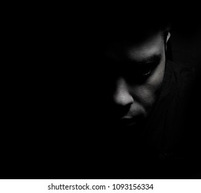 Young man close up portrait, with llong shadow on black background lowkey.