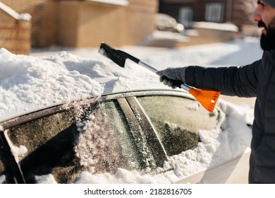 A young man in close-up cleans his car after a snowfall on a sunny, frosty day. Cleaning and clearing the car from snow on a winter day. Snowfall, and a severe snowstorm in winter. - Powered by Shutterstock